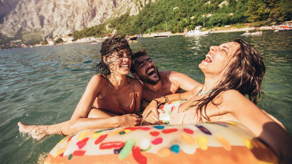 1 A woman lays on an tube float in a lake while a man and another woman laugh.