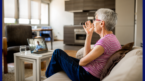 An older woman talks with a therapist during a teletherapy session while sitting on a couch looking at an iPad on a coffee table.